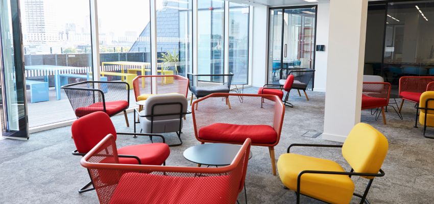 Open room with wall of windows on left hand side. Room is filled with red and yellow comfortable chairs. A recharge space.