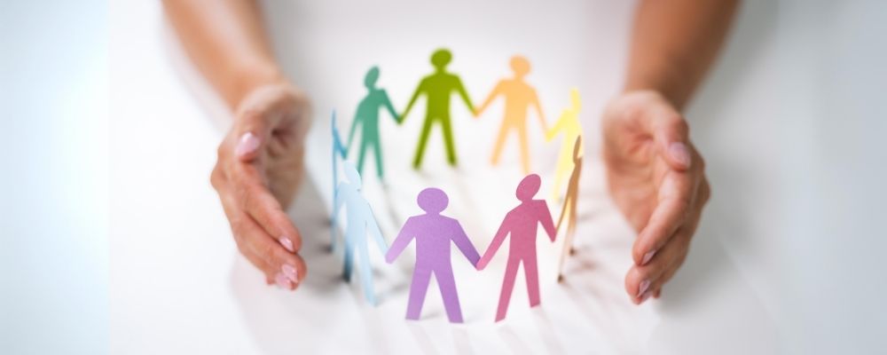 Image of two hands on a white surface surrounding a circle of paper cutouts. Each cutout is a different color and they are connected by the hands.